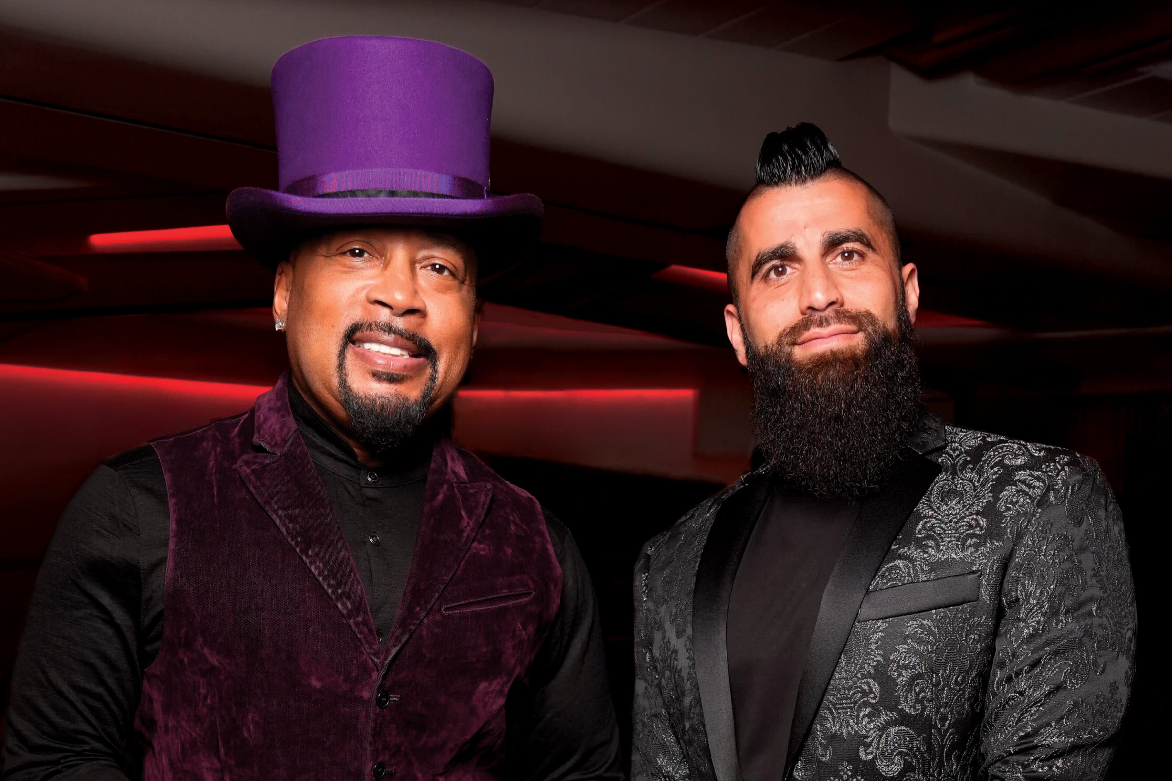 Daymond John and Robert Rivani in formal attire standing together at an upscale venue with red lighting in the background