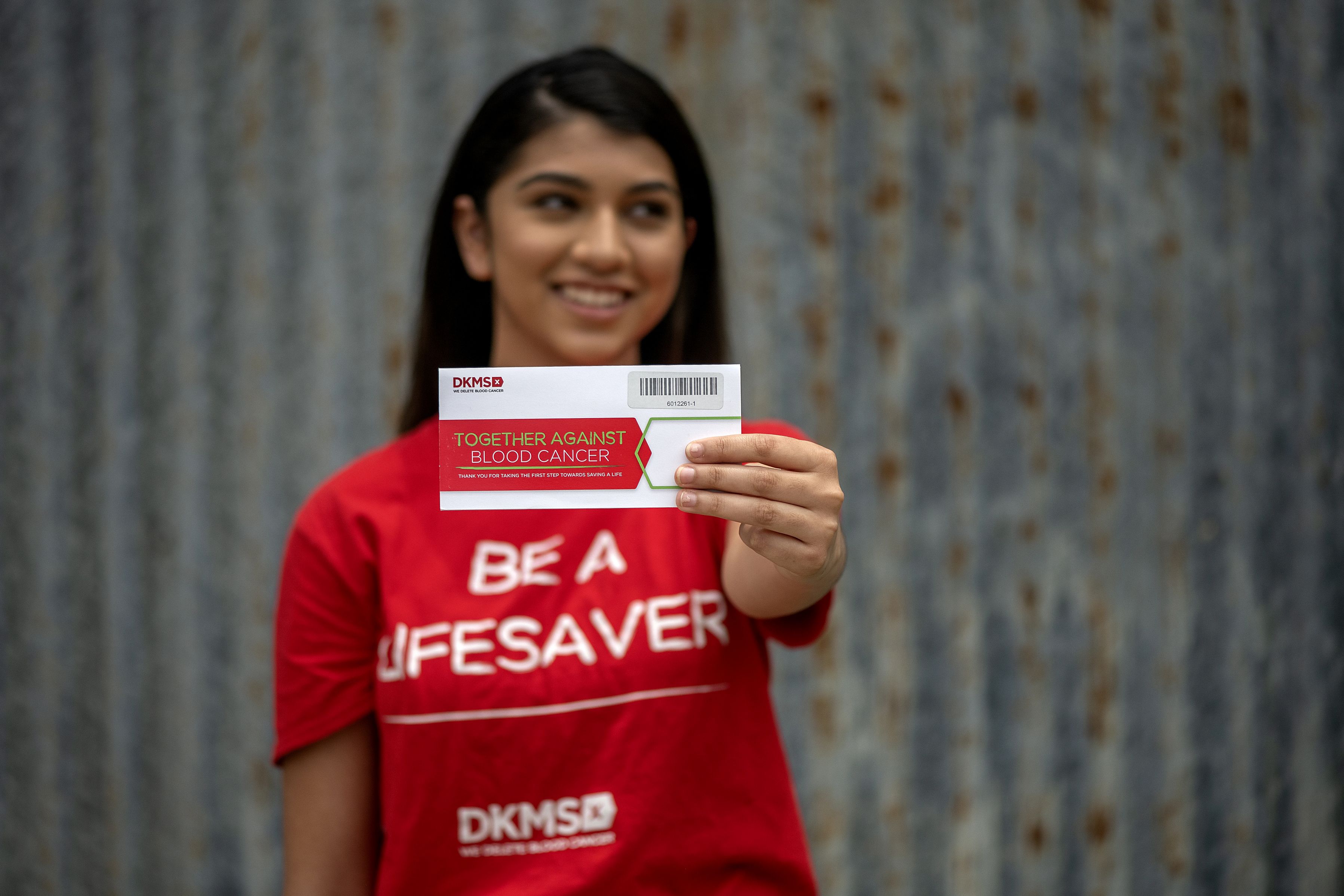 Woman in a red DKMS shirt holding a DKMS “Together Against Blood Cancer” envelope.