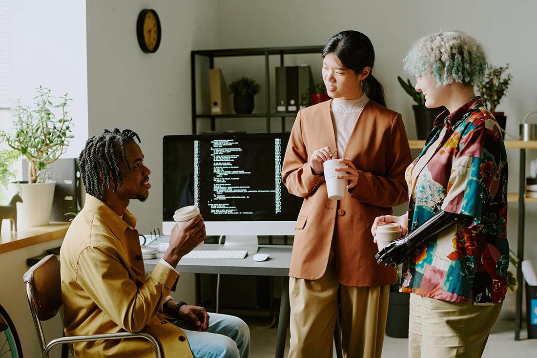 Group of three diverse gen Z colleagues wearing stylish outfits chatting during coffee break in office