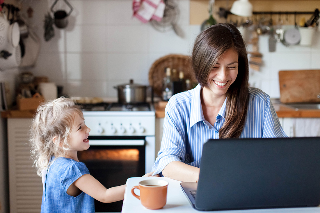 Working mom works from home office. Happy mother and daughter smiling. Successful woman and cute child using laptop. Freelancer workplace in cozy kitchen. Female business. Lifestyle authentic moment.