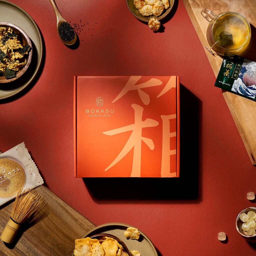 product image of orange Bokksu box surrounded by oils and other snacks