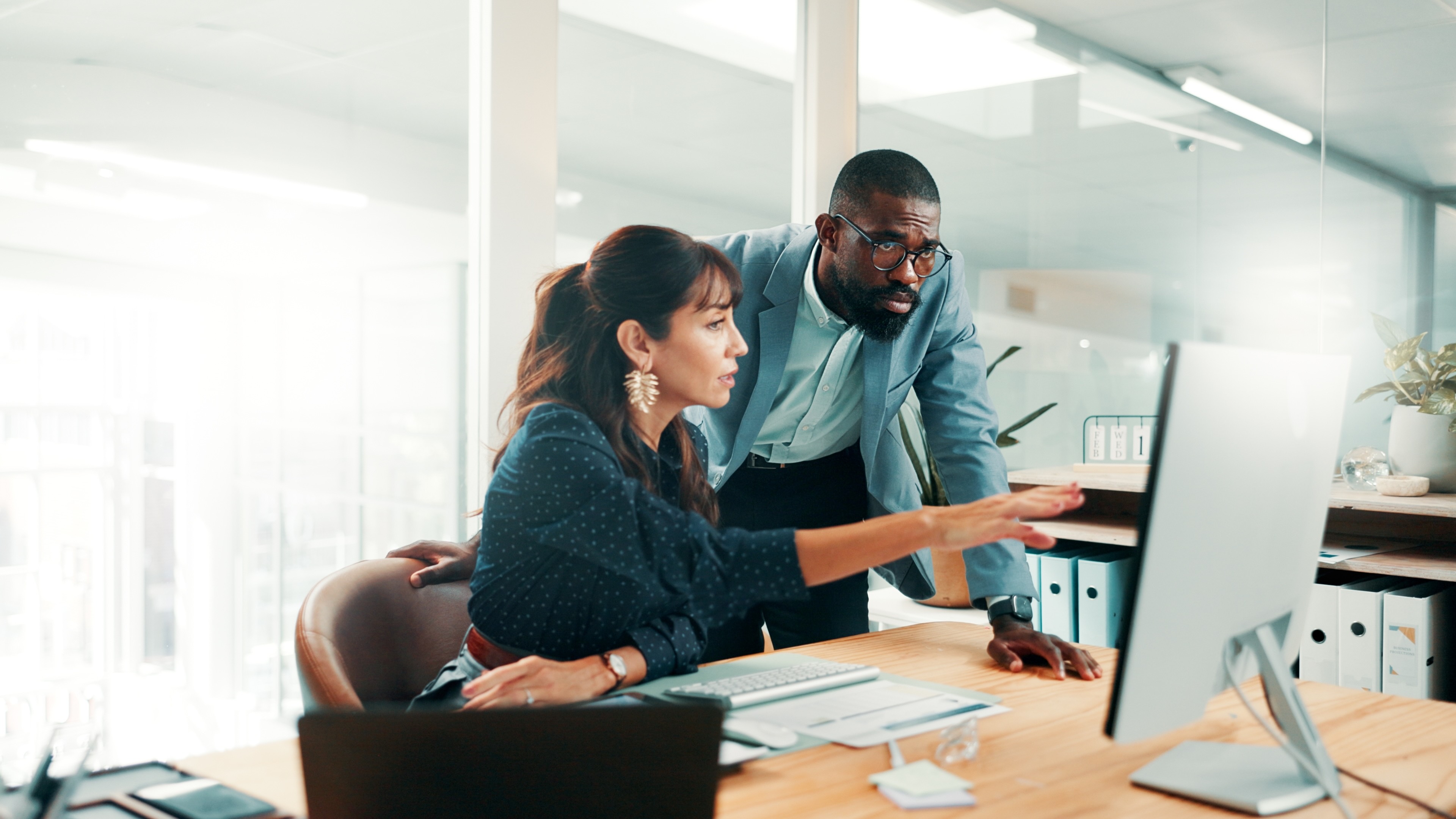 Two professionals reviewing work on computer screen together in modern office