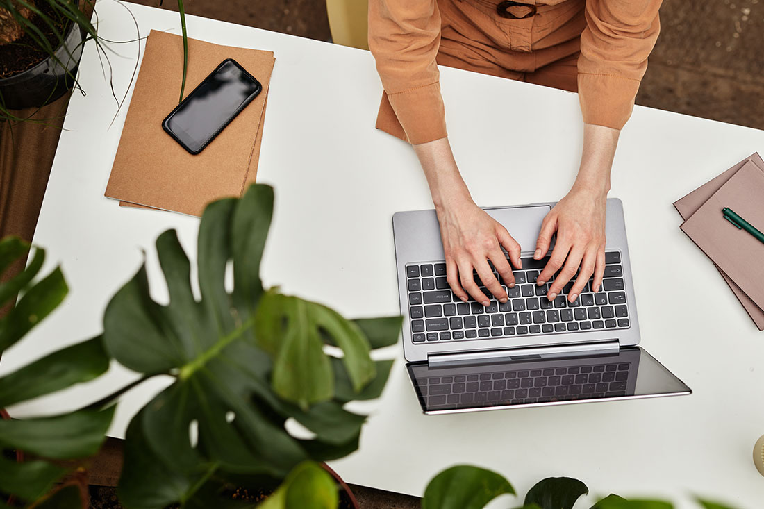 Overview of hands of young businesswoman or student typing on laptop keyboard by desk