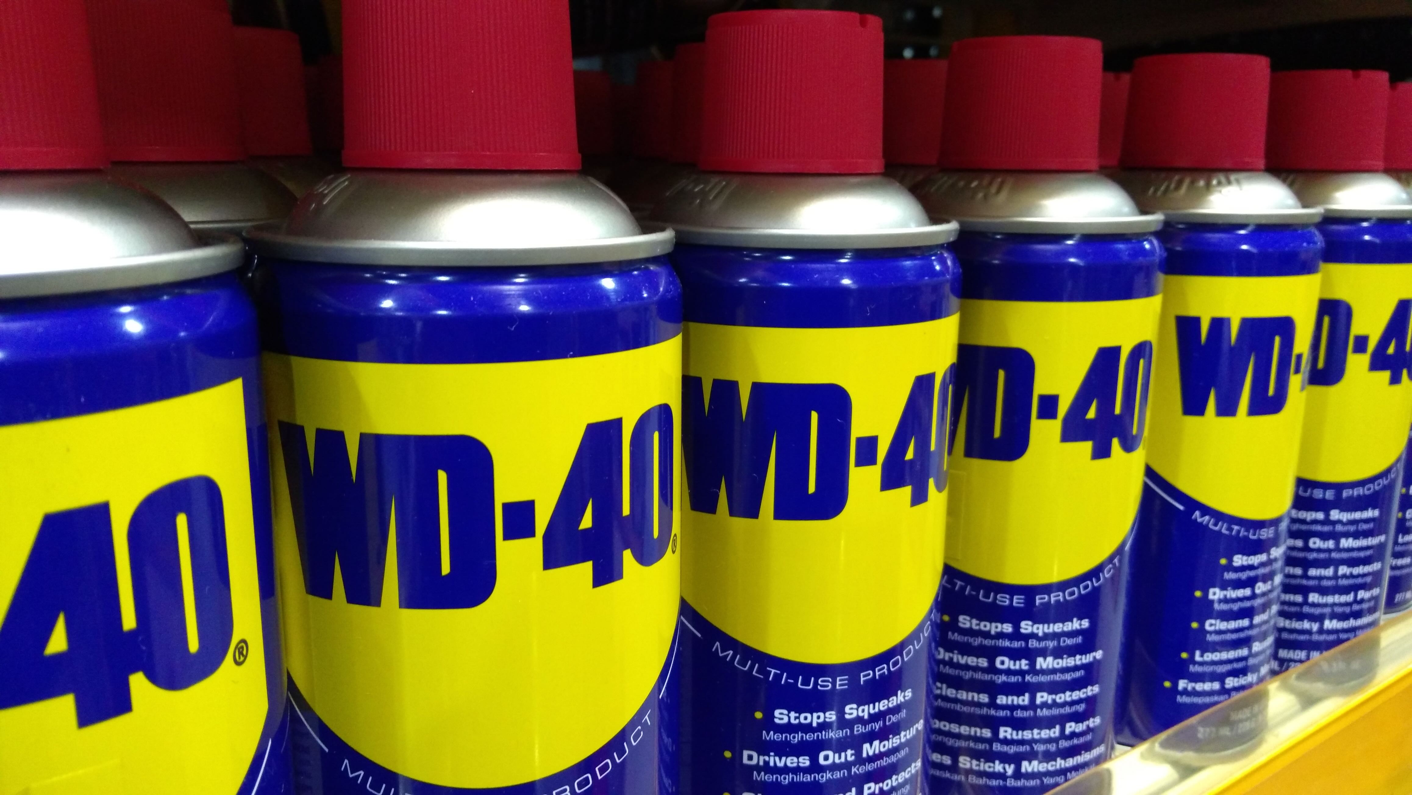 Row of WD-40 cans with iconic blue and yellow labels and red caps lined up on a store shelf