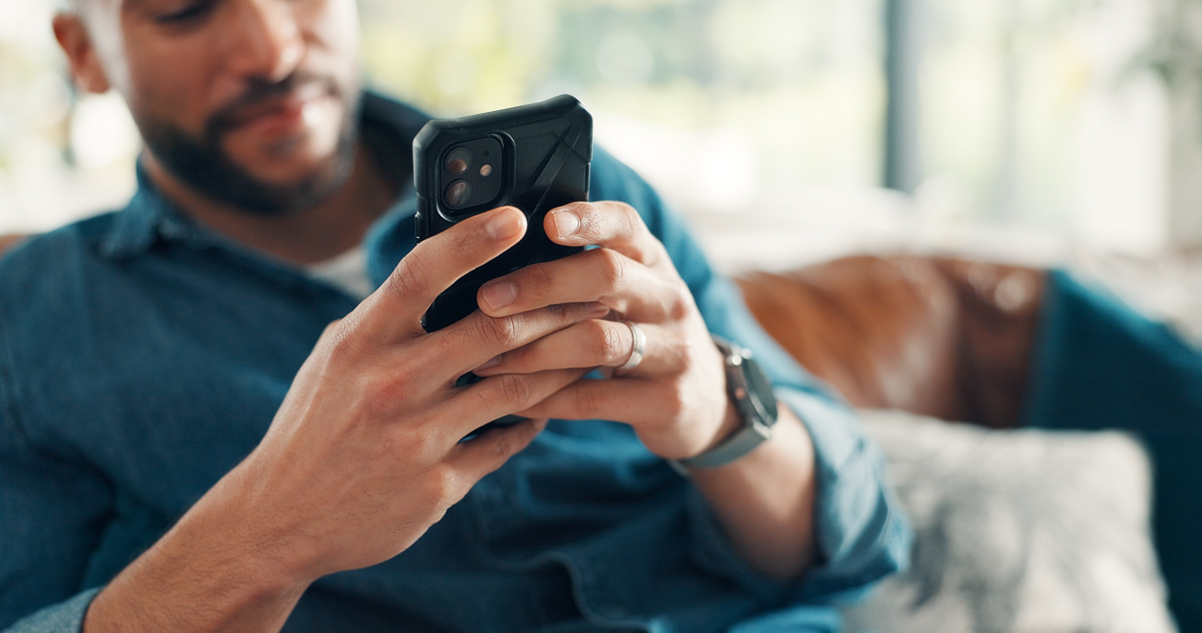 Man in blue shirt holding smartphone while setting boundaries through text message