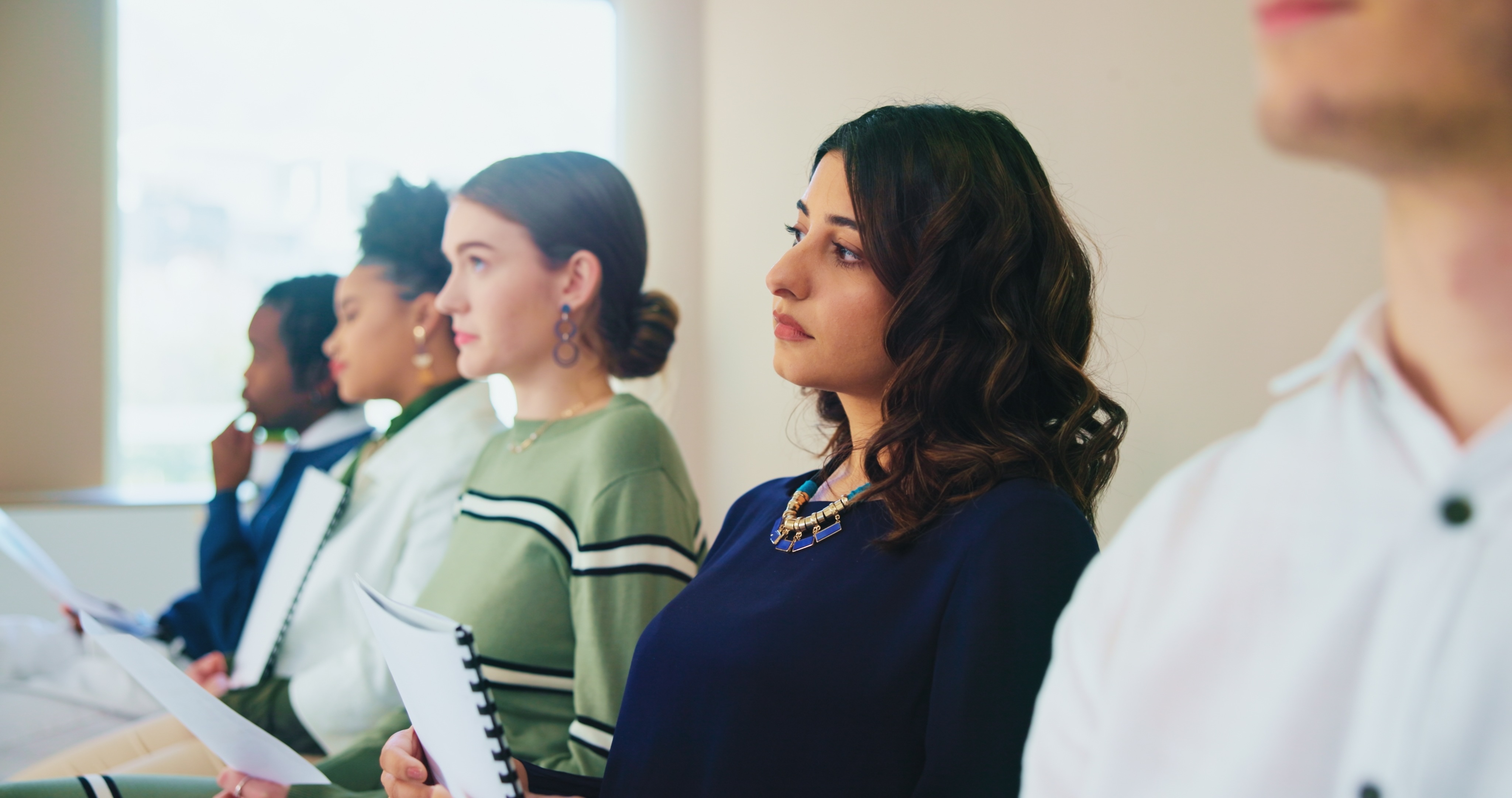 Young professionals holding notepads attentively listen during a workplace meeting or interview
