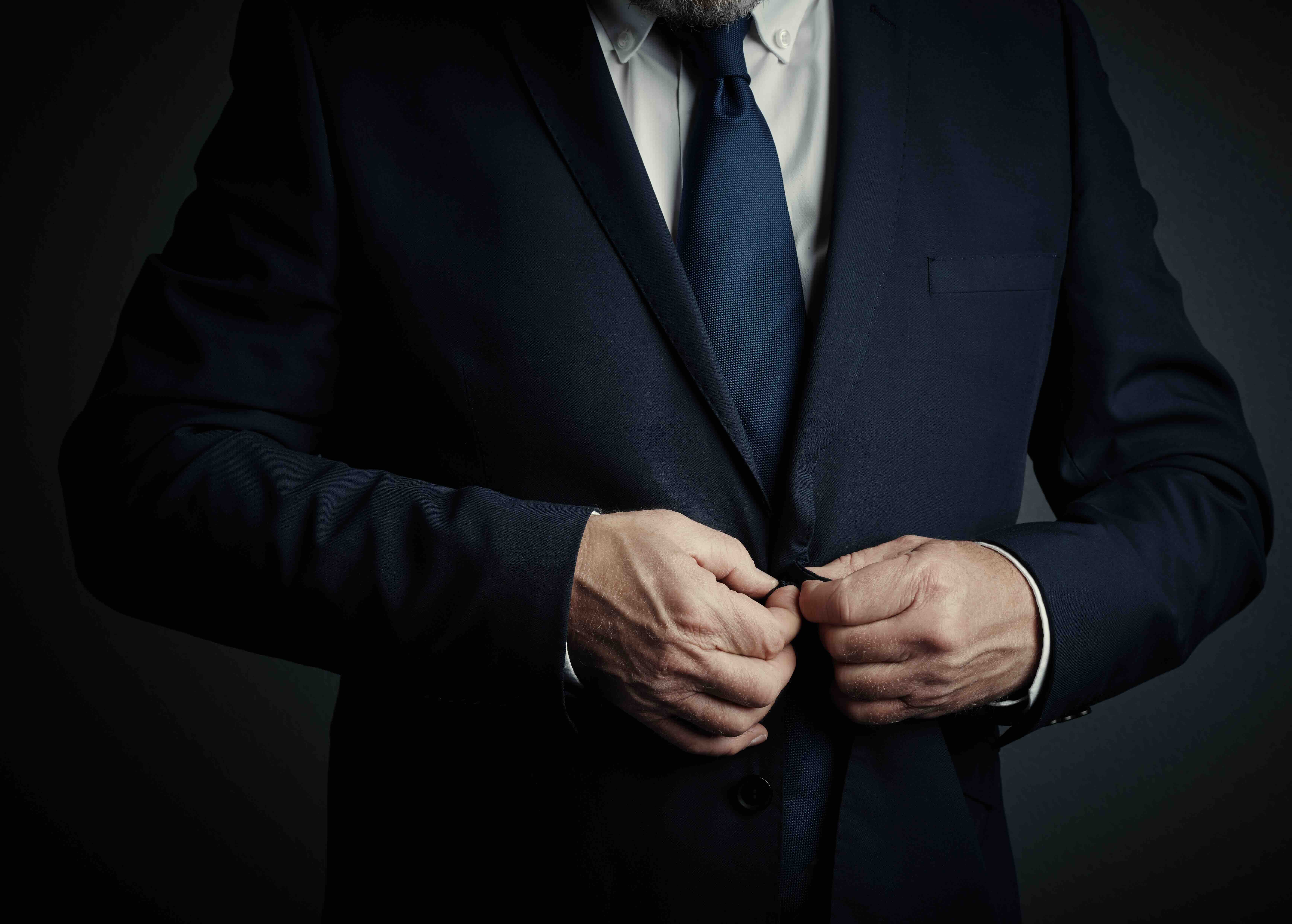 Professional in navy suit buttoning jacket while wearing white dress shirt and blue tie