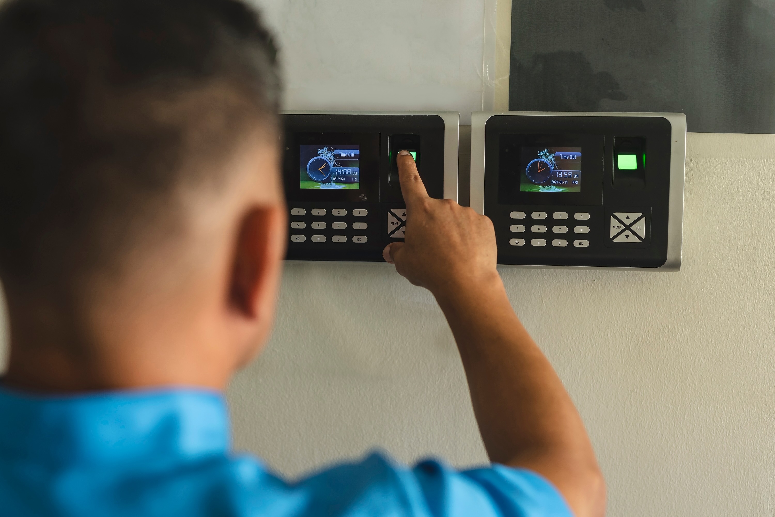Person using fingerprint scanner on time clock displaying work hours clocked in and out