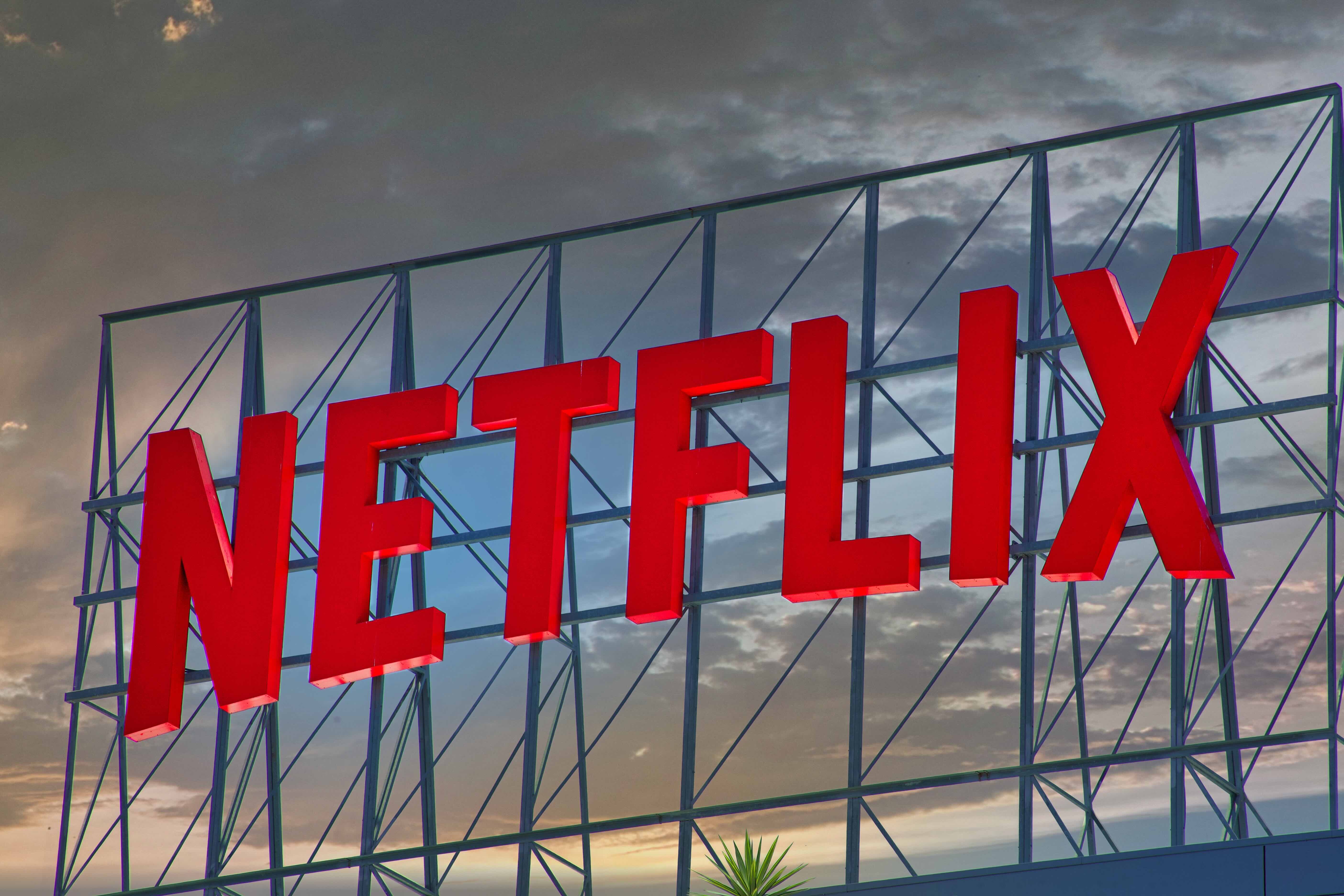 Large red Netflix sign mounted on metal scaffolding against a cloudy sky at dusk