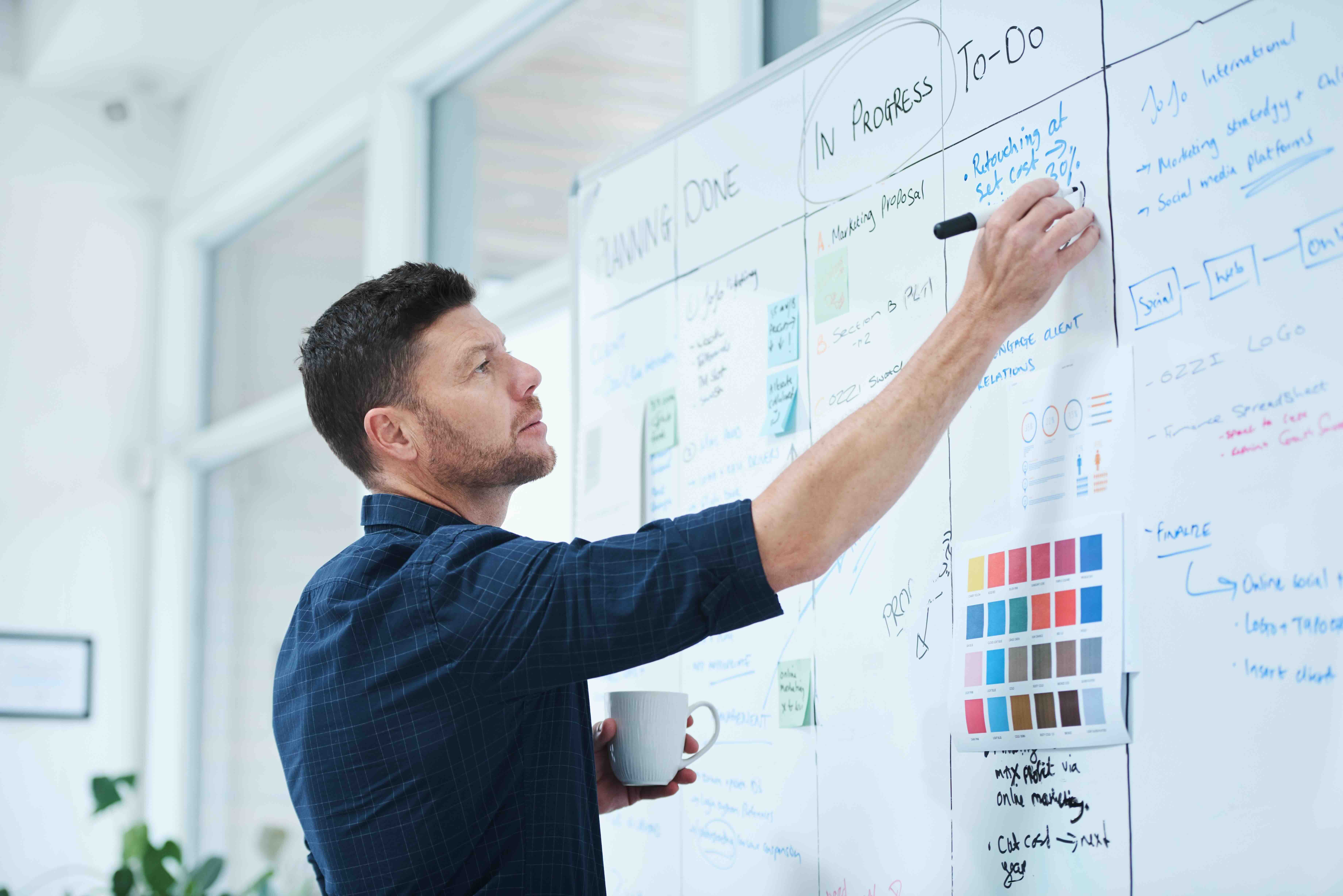 Man writing on whiteboard while holding coffee cup during strategic planning session