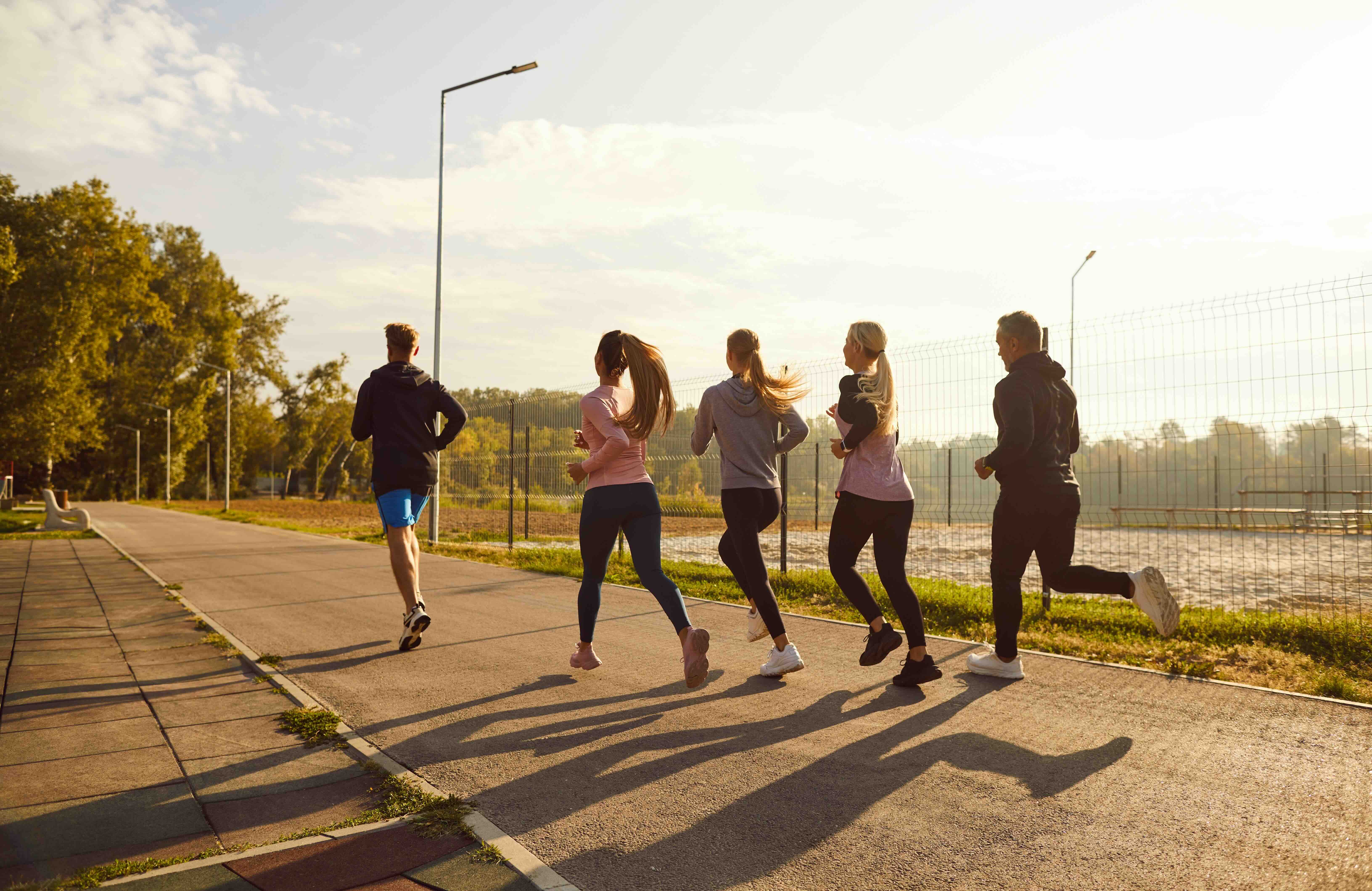 Group of five runners jogging together on a paved path during golden hour near sports courts