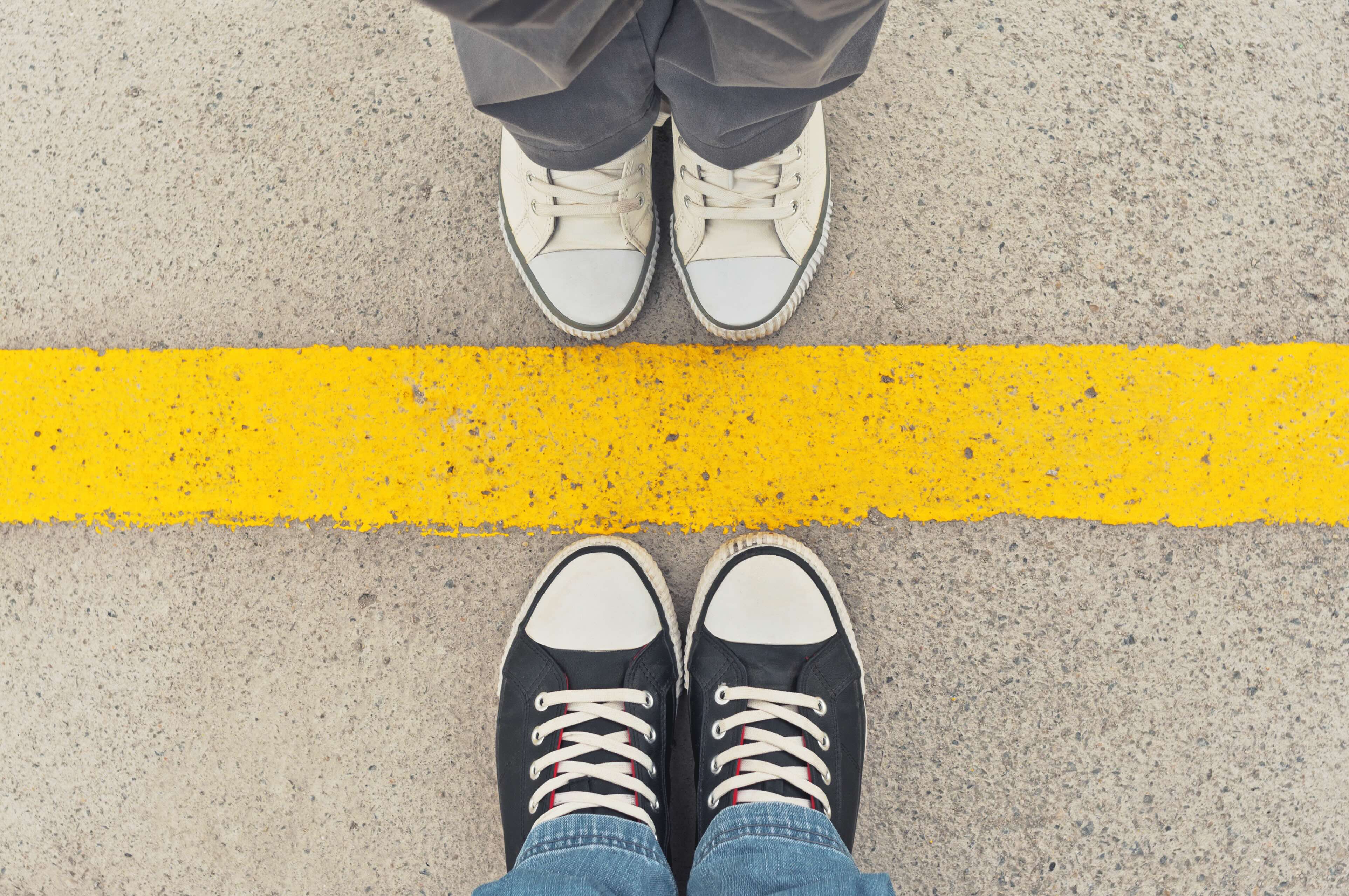 Two people standing on opposite sides of a yellow boundary line on pavement