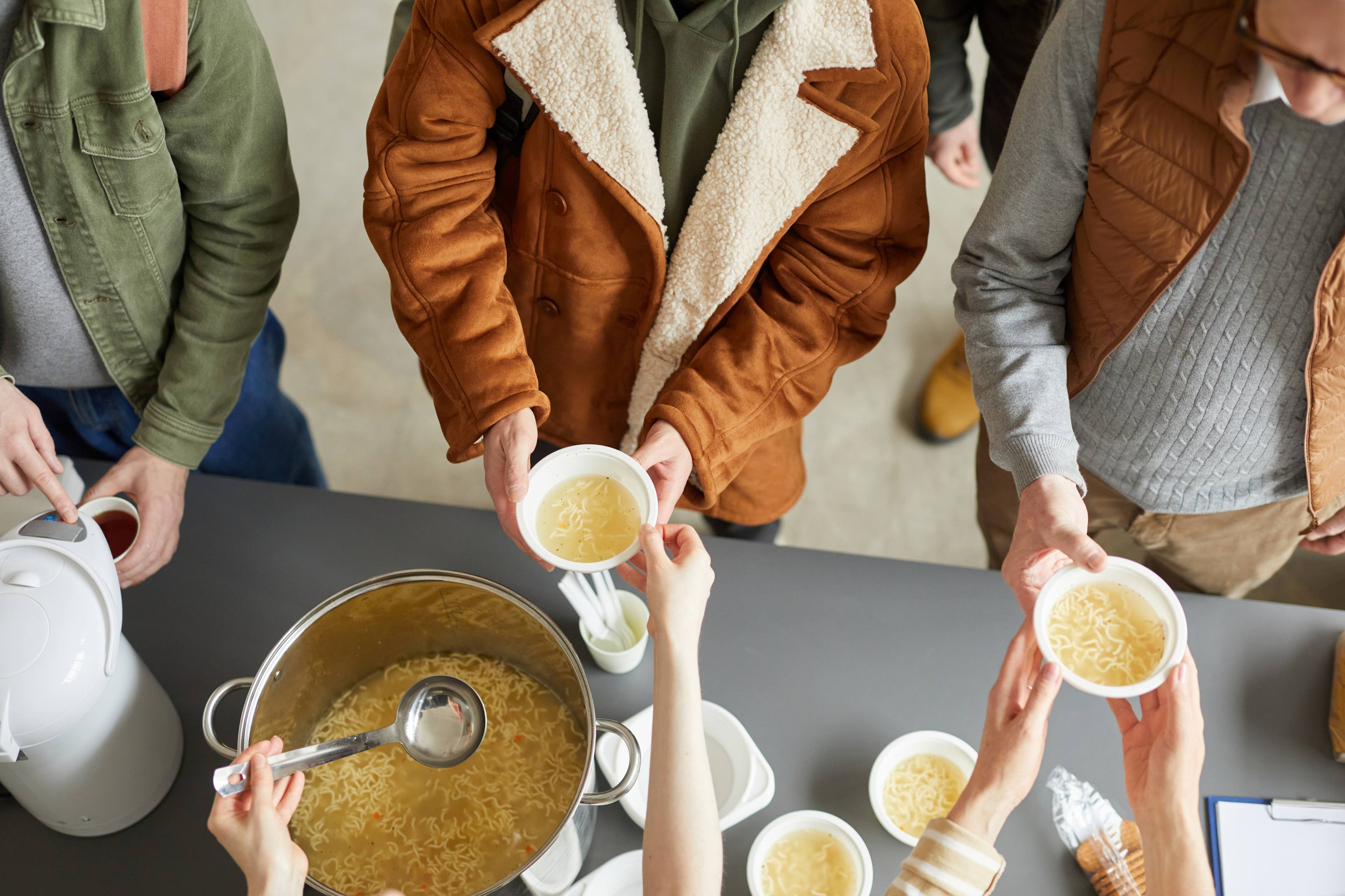 Group of people serving soup from large pot into bowls demonstrating community care and volunteering
