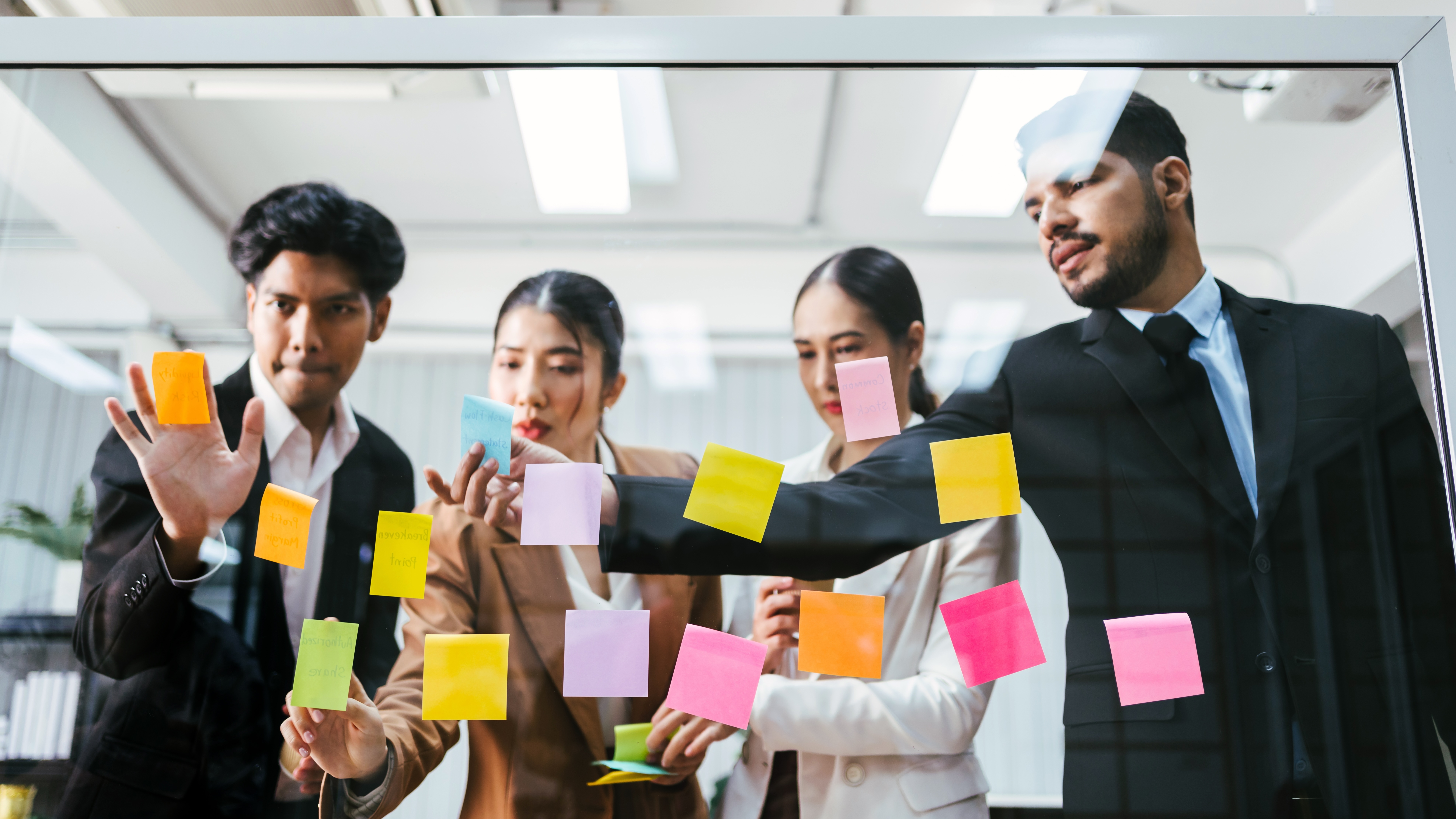 Four business professionals in suits collaborating with colorful sticky notes on a glass board