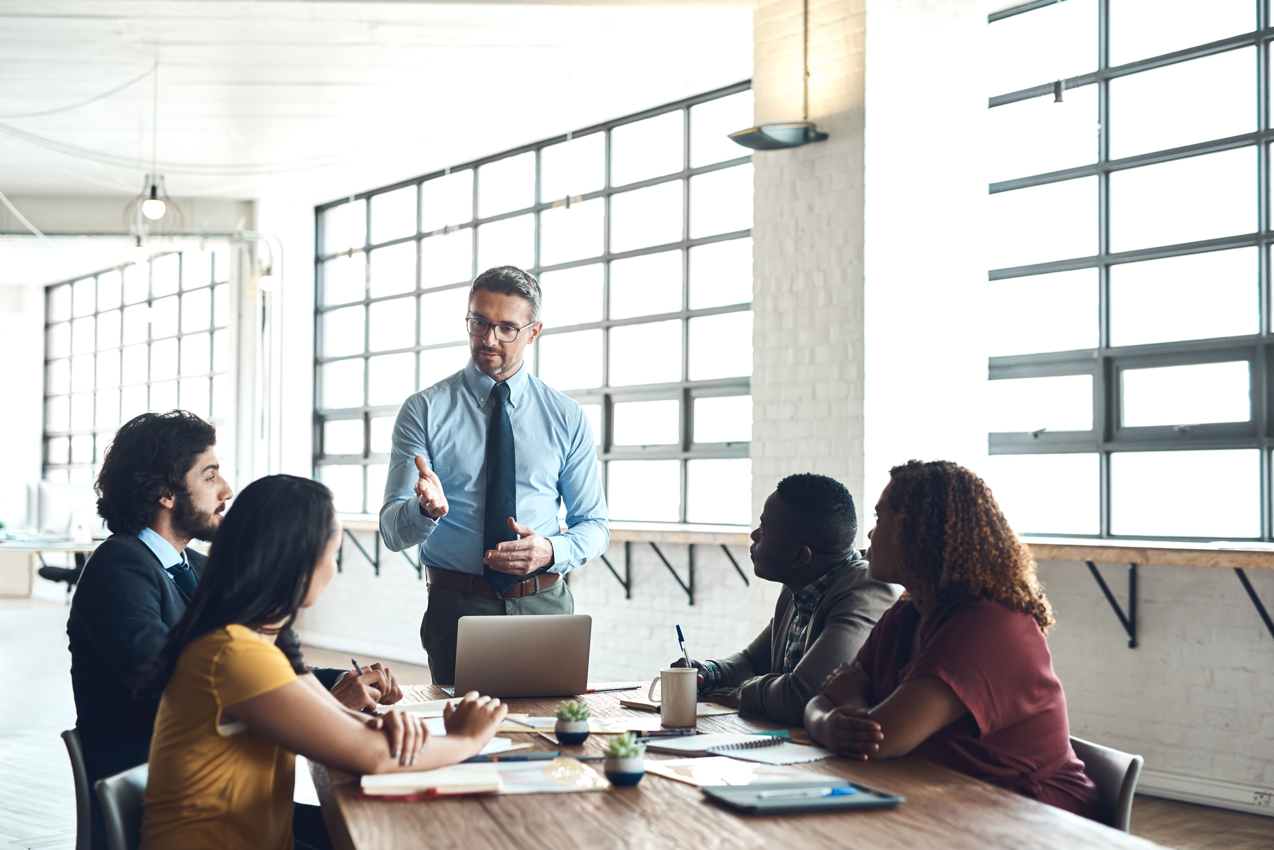 Business leader standing and presenting to diverse team seated around conference table in modern office
