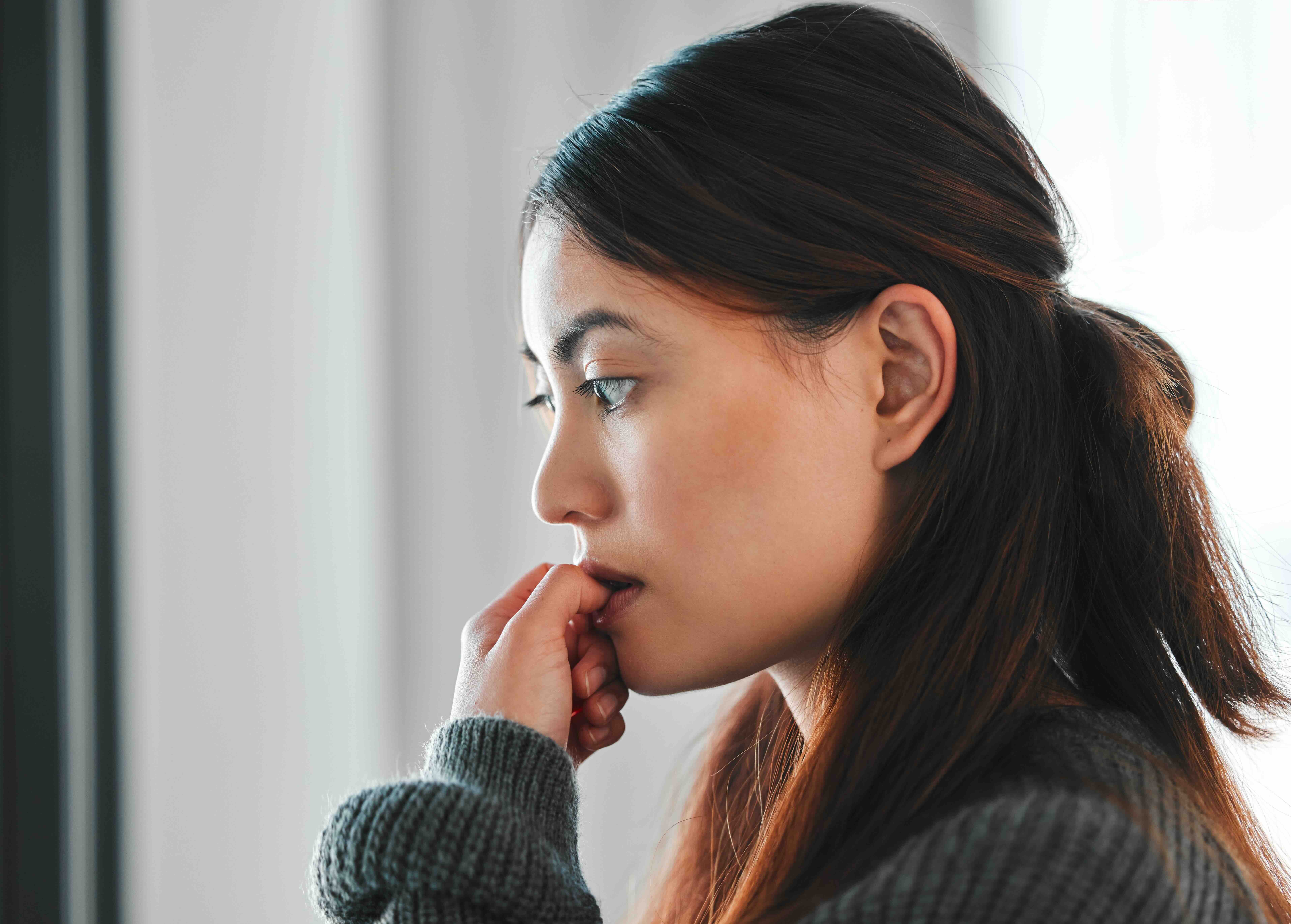Woman in gray sweater looking thoughtfully to the side with hand near face in contemplative pose