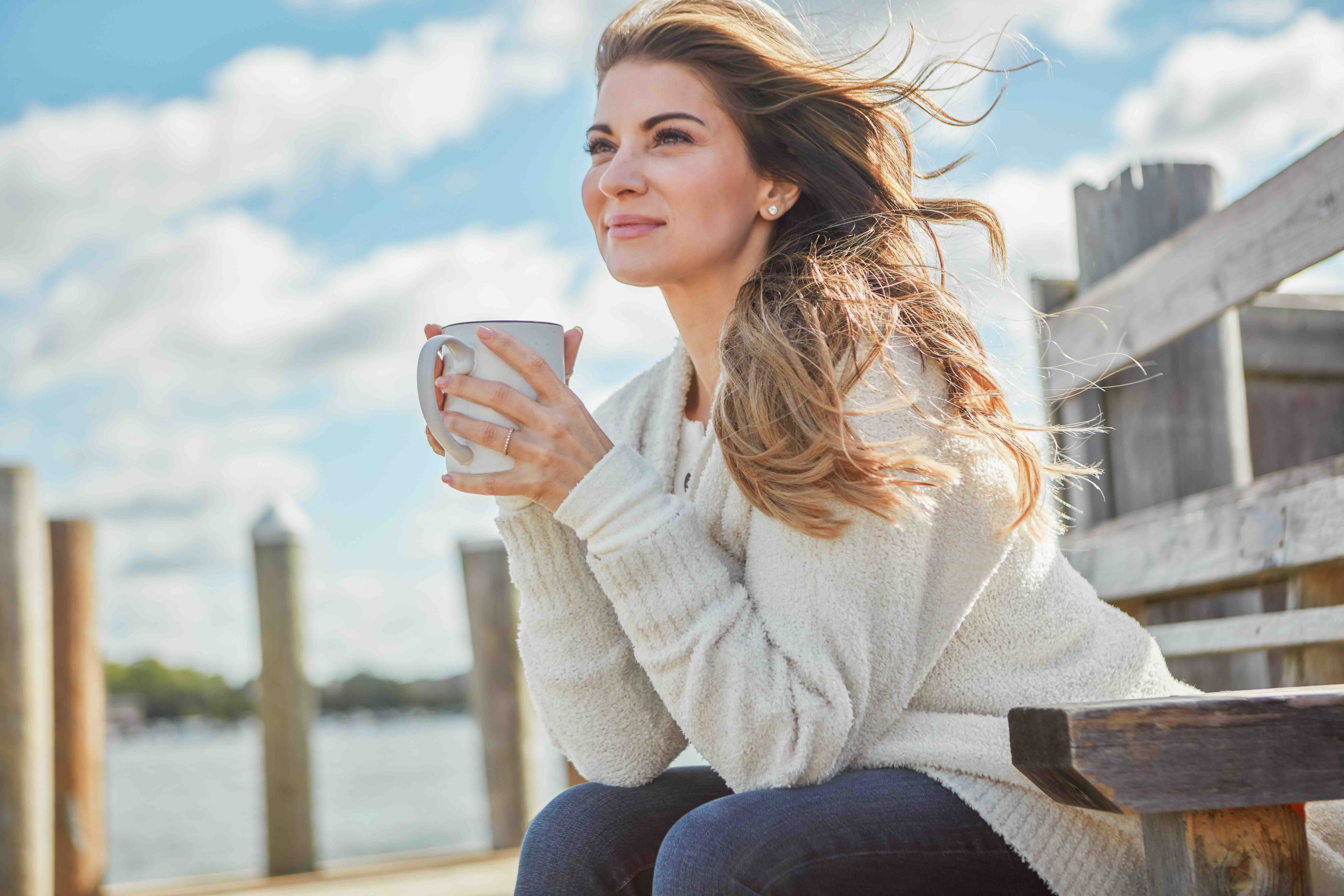 Woman with coffee cup on pier, positive mindset