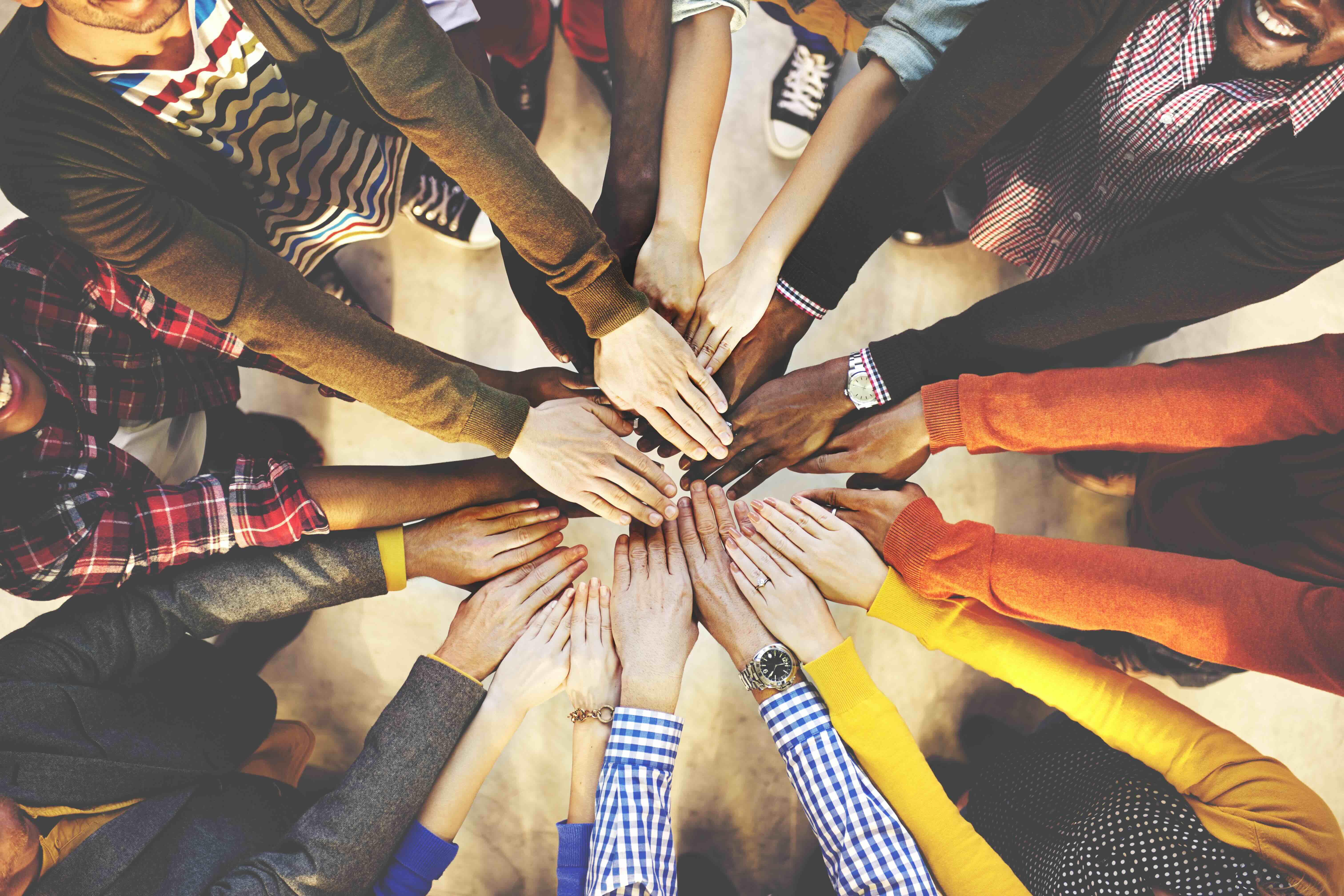 Diverse group of people stacking hands together in a circle showing teamwork and unity