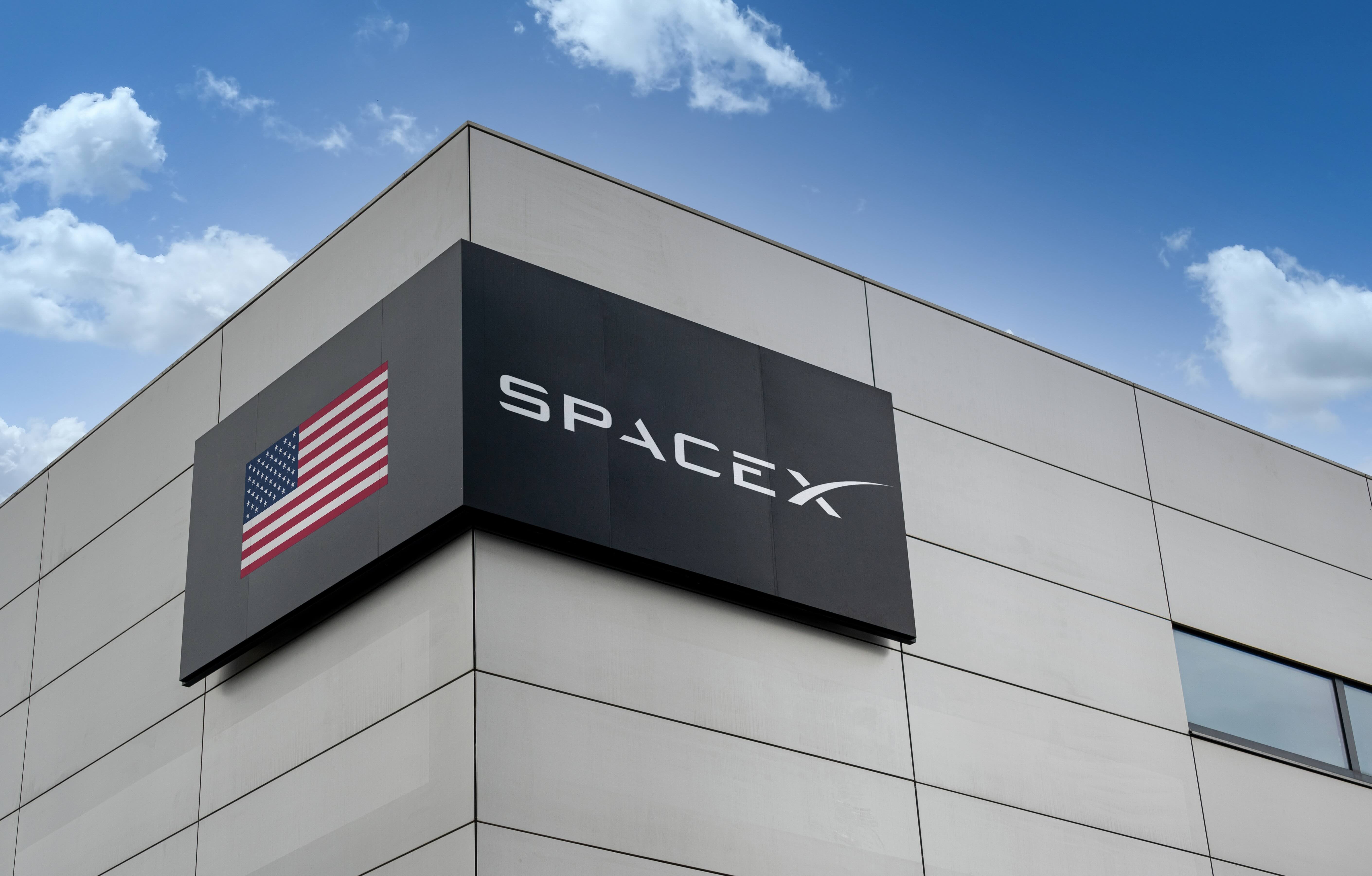 SpaceX logo and American flag displayed on corner of modern gray building facade under blue sky