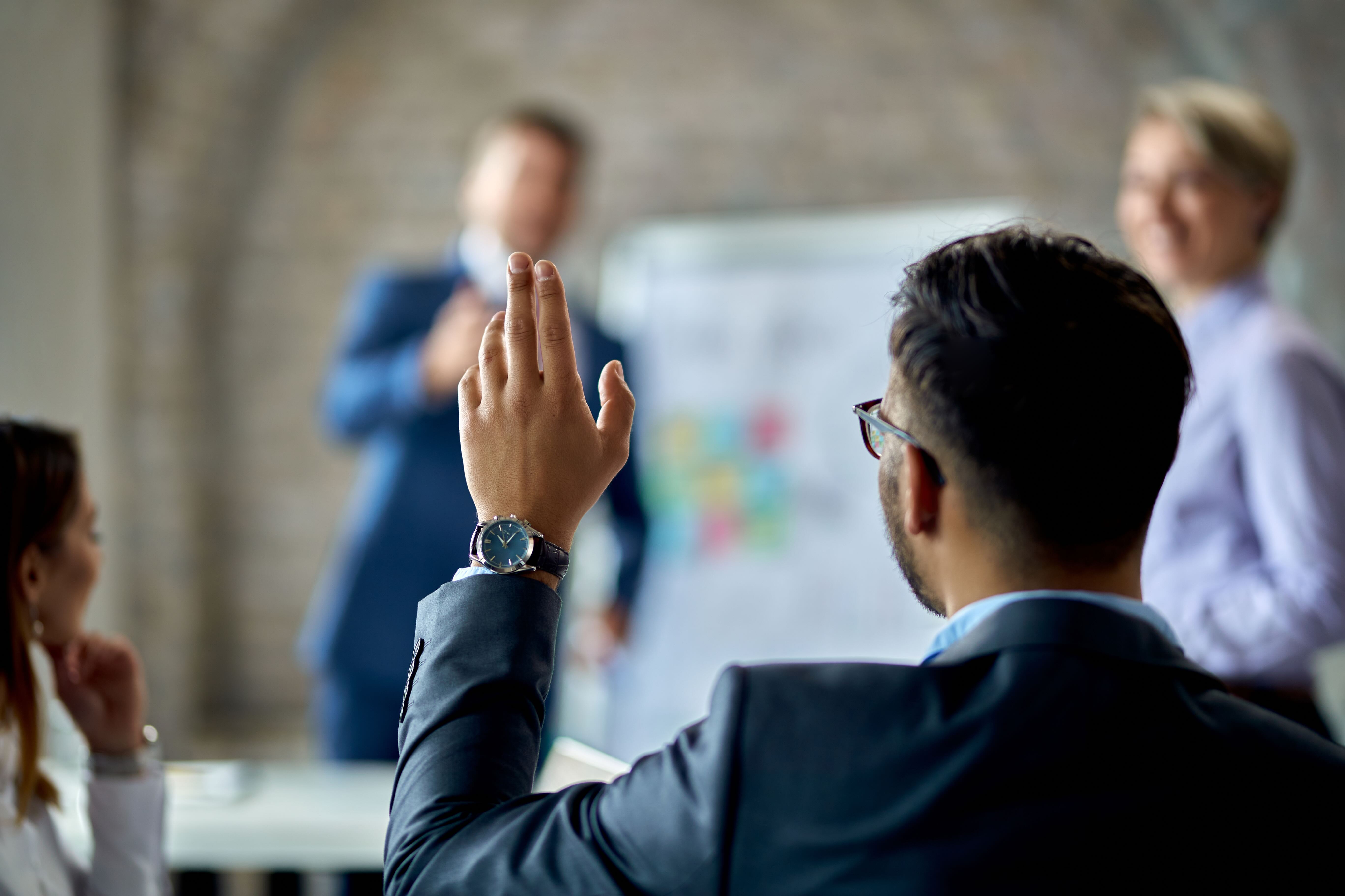 Business professional raising hand to ask question during office meeting presentation