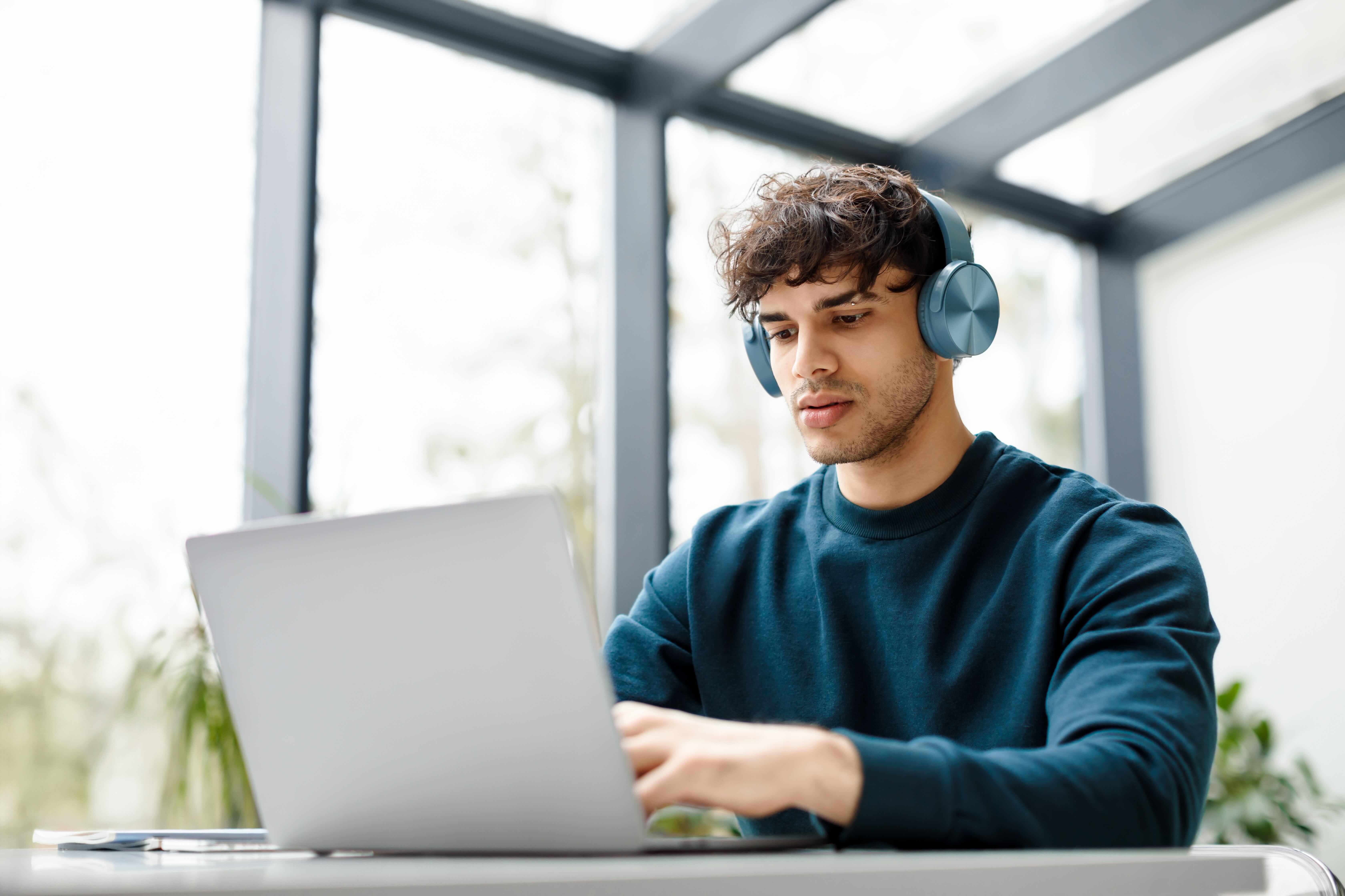 Man wearing headphones working focused on laptop in bright modern office space