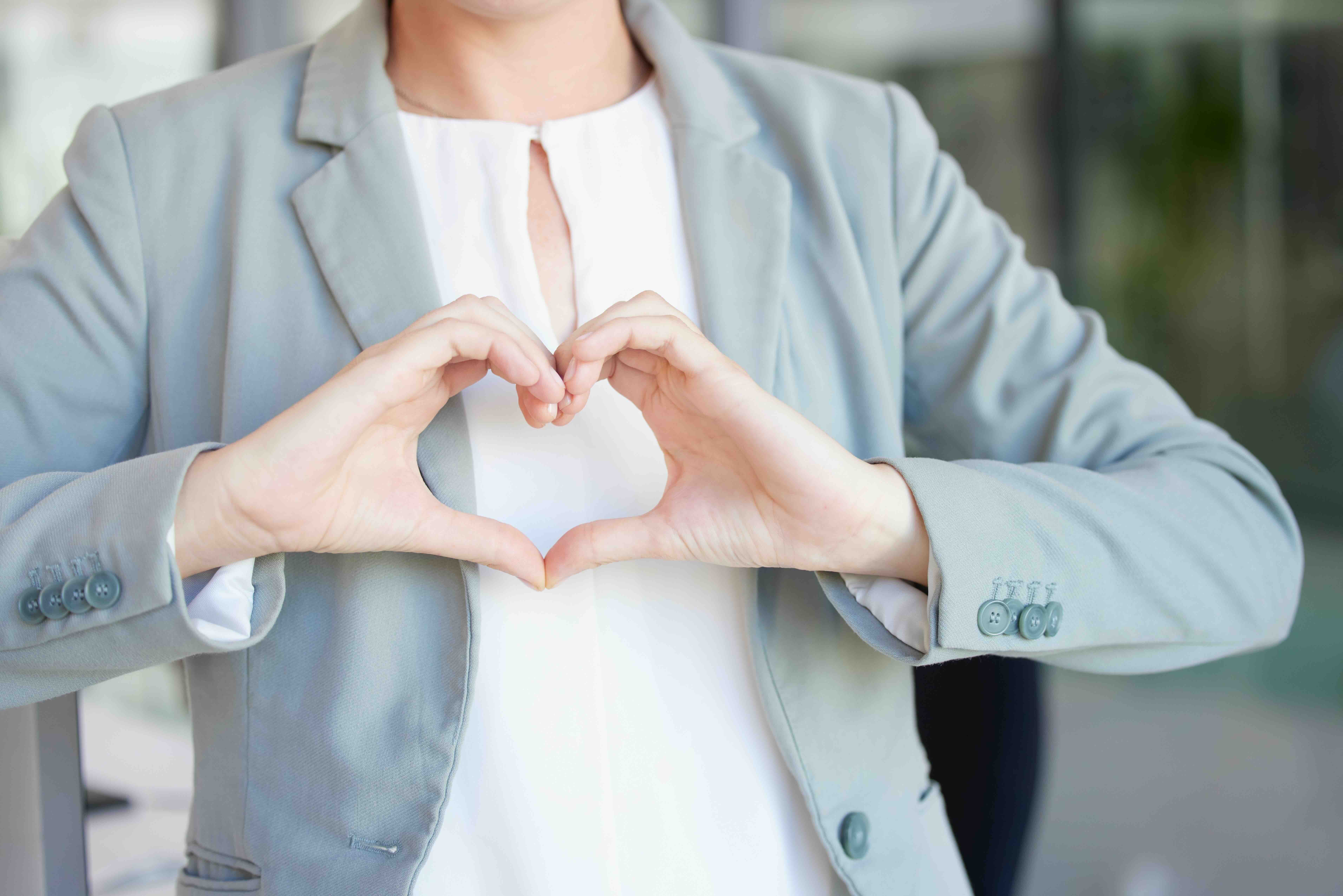 Professional woman in light blue blazer making heart shape with hands over chest