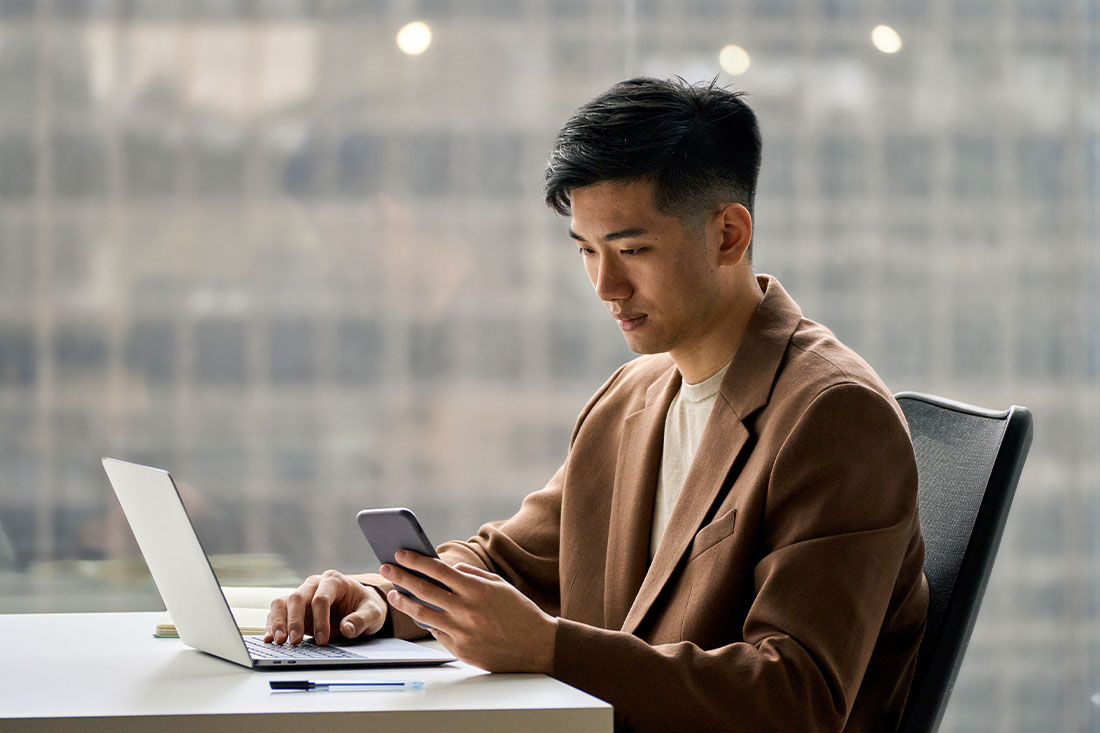 Man using cell phone looking working in corporate office with laptop computer