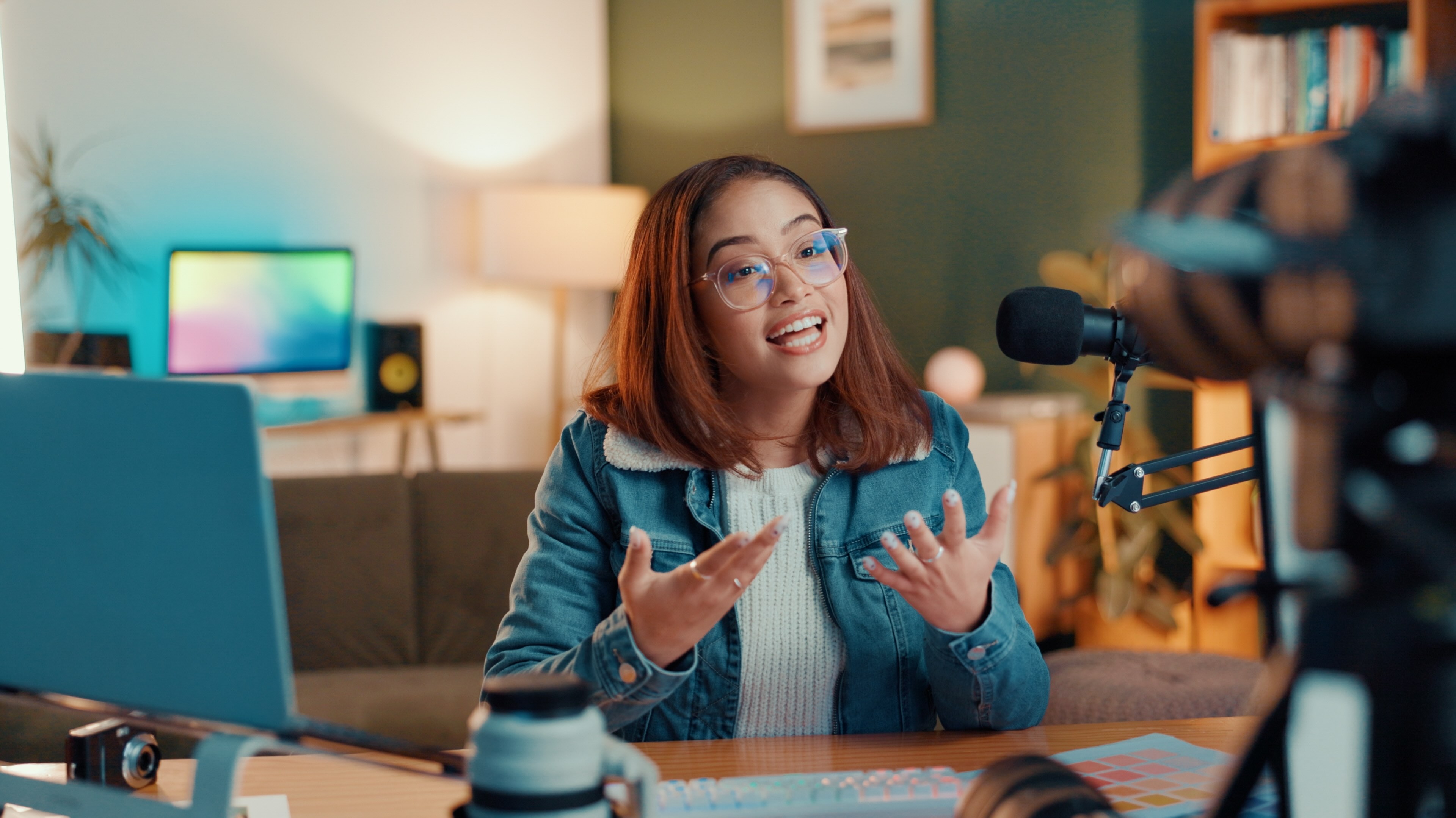 Content creator filming herself speaking to camera with microphone and laptop in home studio setup