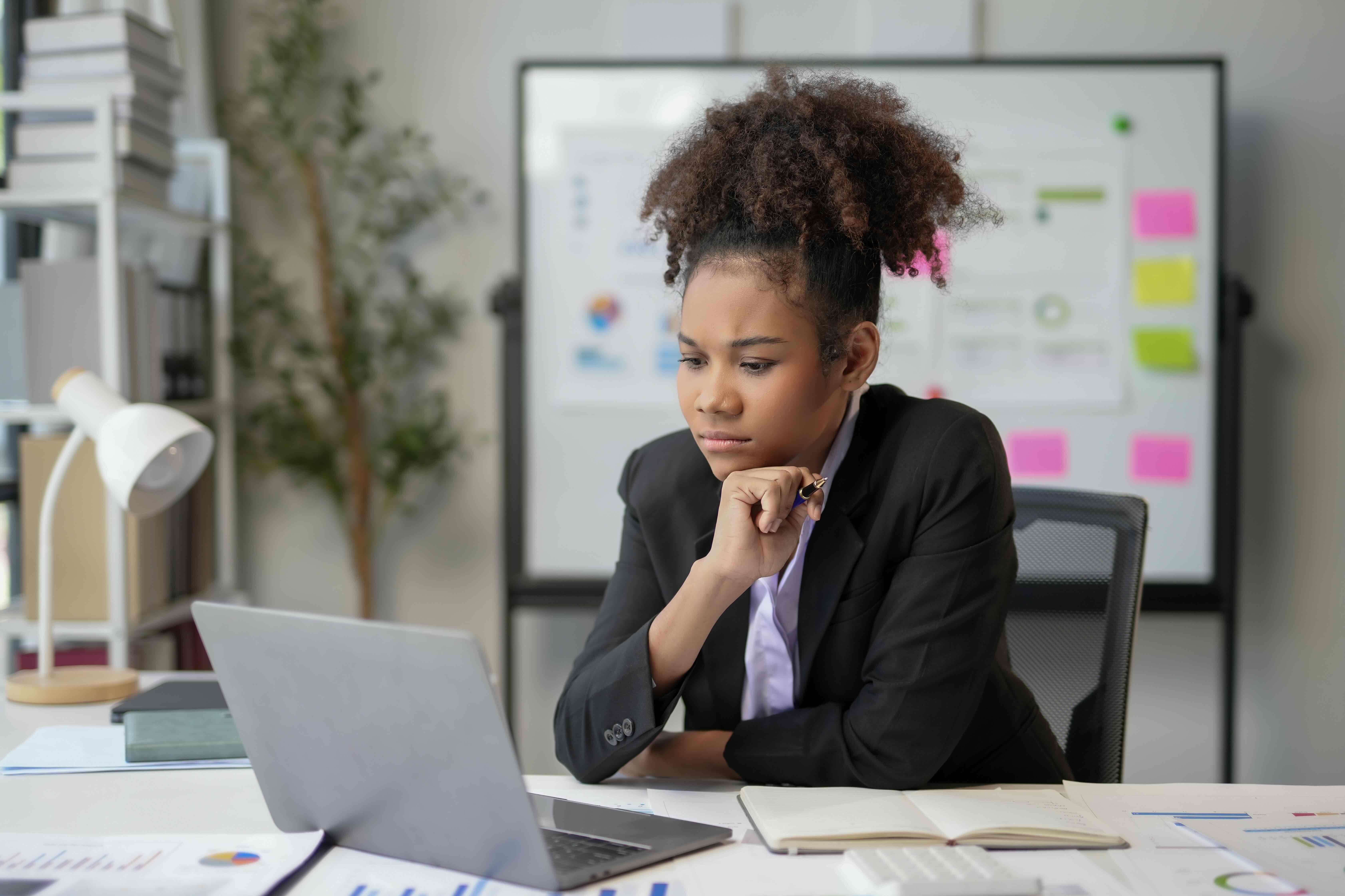 Professional woman in business attire concentrating intently while working on laptop at modern office desk