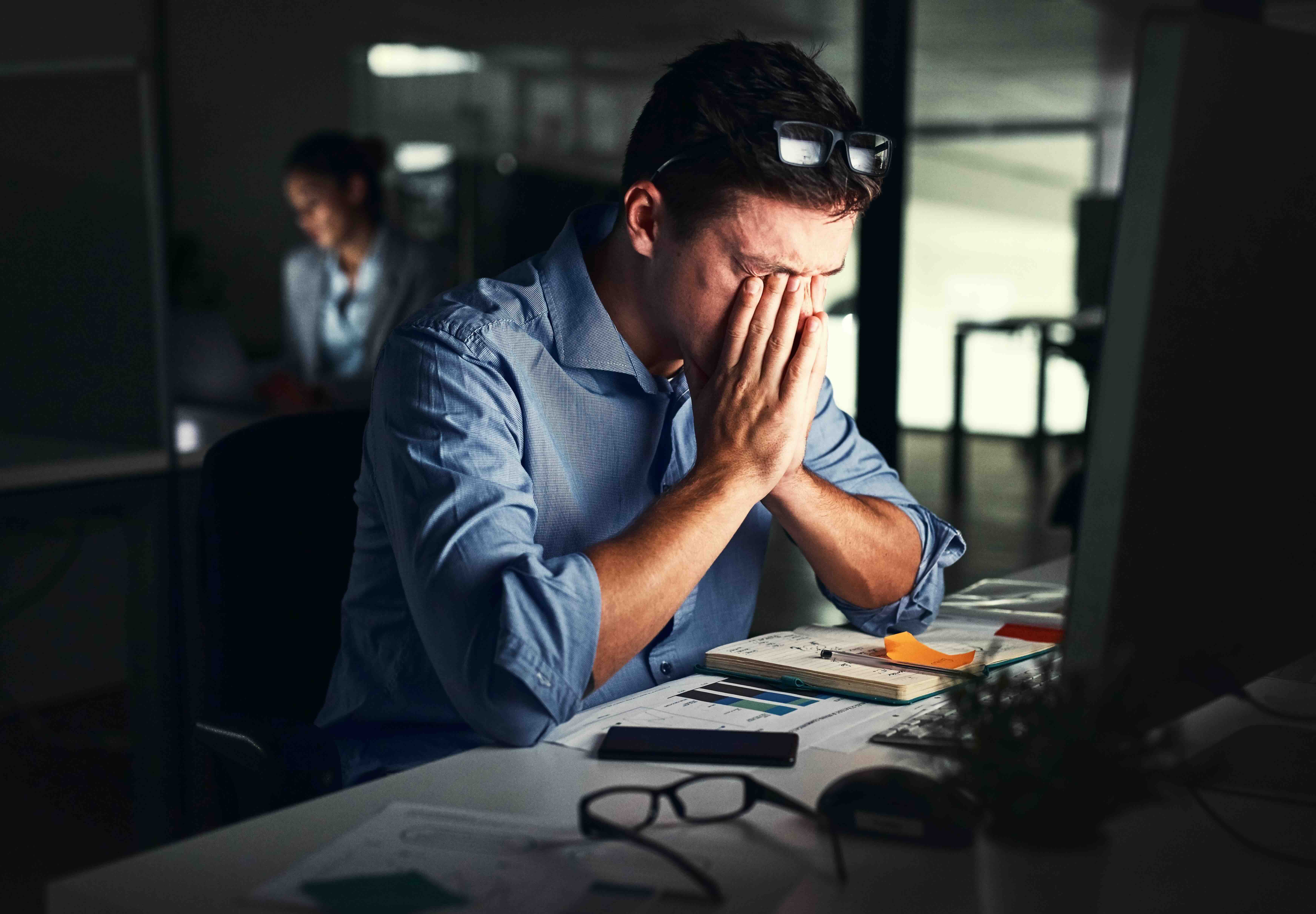 Stressed businessman at desk with hands covering face showing signs of burnout and exhaustion