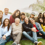Happy intergenerational friends having fun sitting on grass in a public park