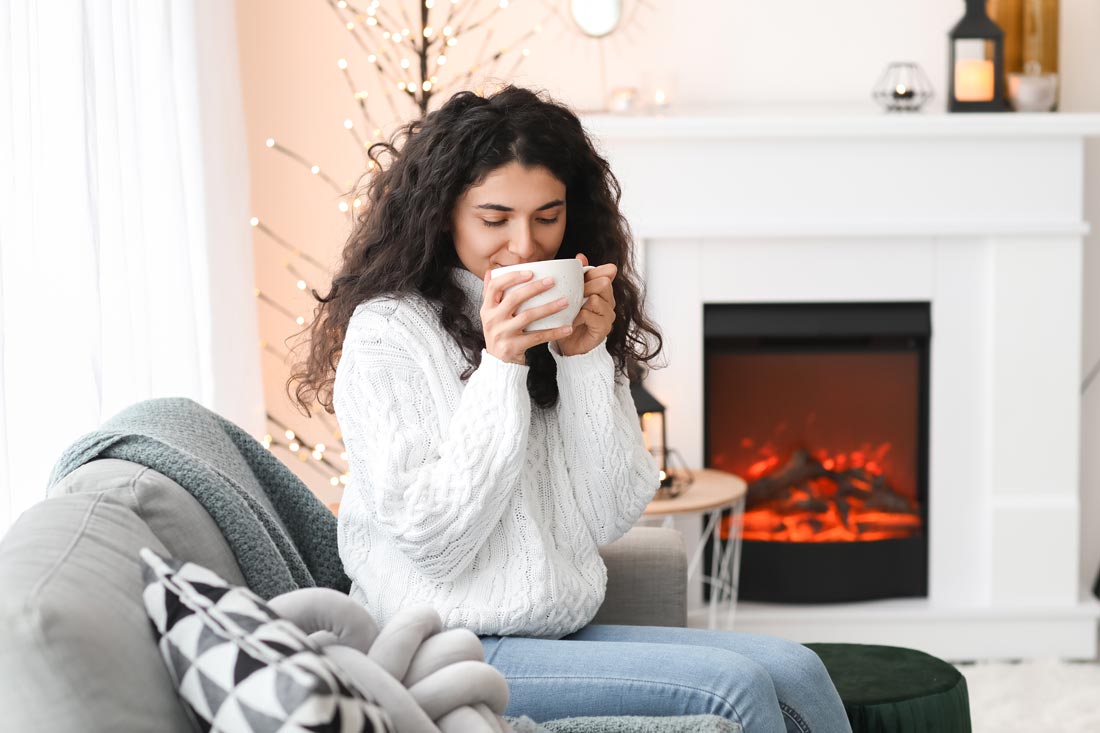 woman drinking tea by fireplace to reduce holiday stress