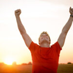 Successful man raising arms after cross track running on summer sunset