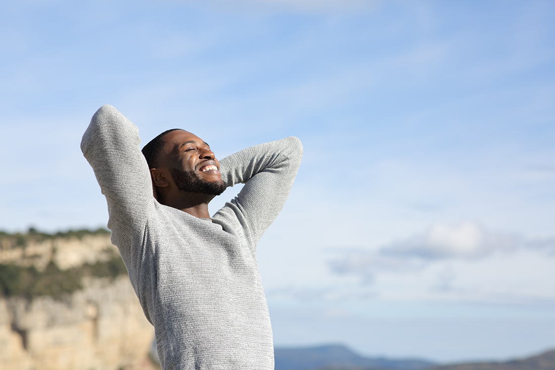 Relaxed man breathing on a mountain, experiencing a blissful morning