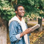 happy millennial man reading book outside