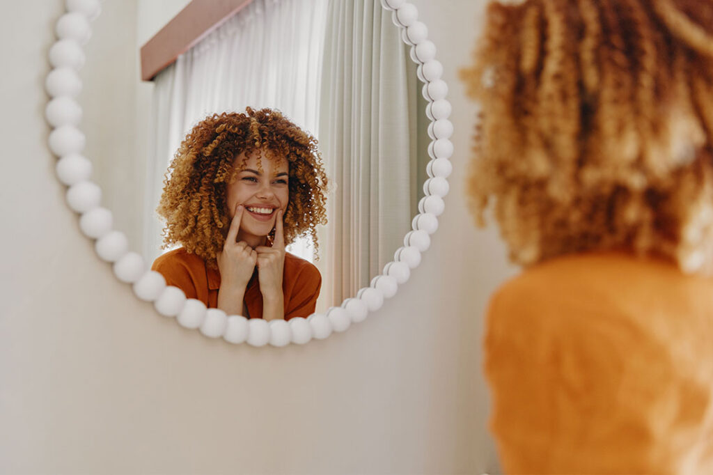Joyful woman with curly hair smiling in mirror