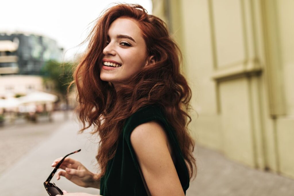 a woman looking over her shoulder and smiling at the camera while holding a pair of sunglasses