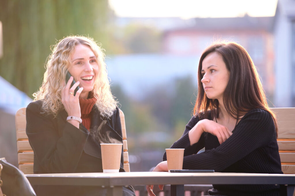 Two women sitting together, one is on the phone and the other is realizing it's time to end the friendship