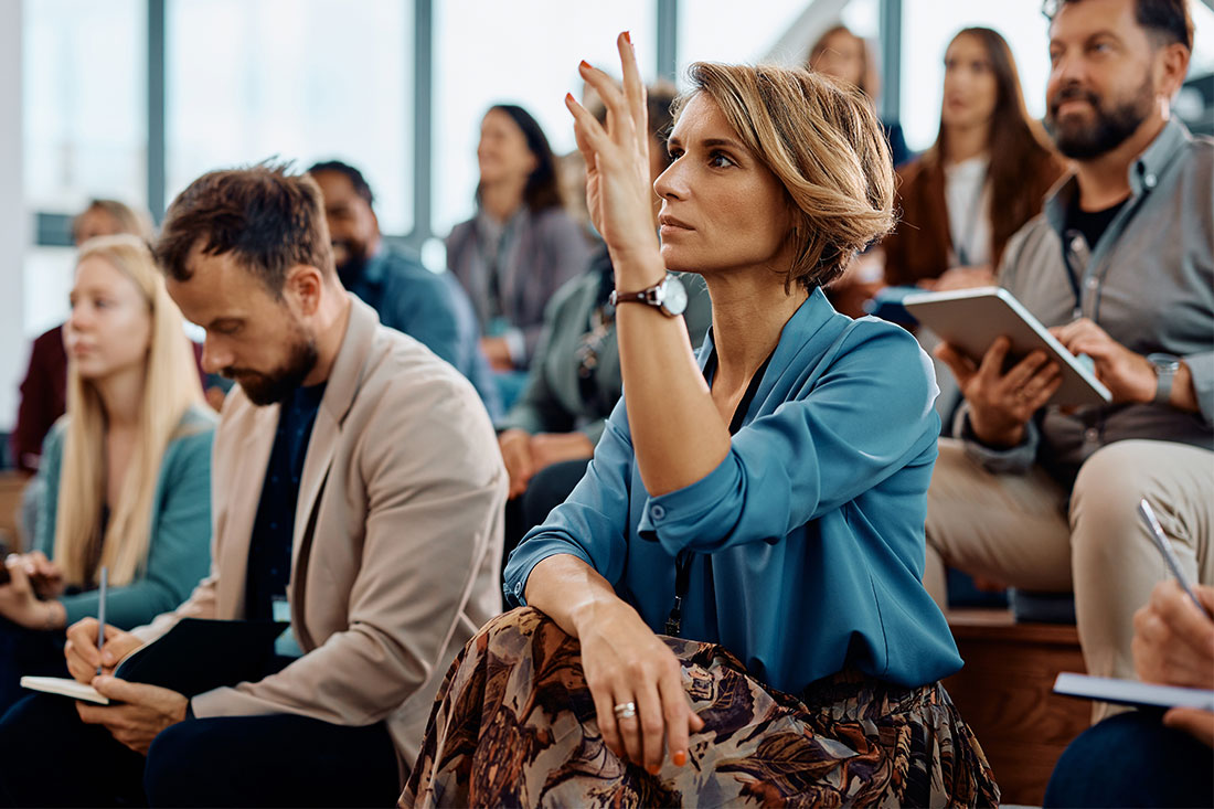 Female entrepreneur raising her hand to answer a question during business conference in convention center