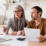 a couple sitting at a table and looking at a laptop to review their finances