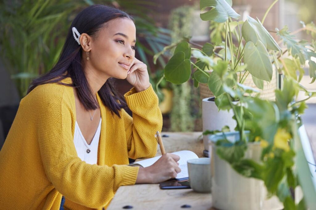Woman writing in her journal surrounded by plants visualizing the future