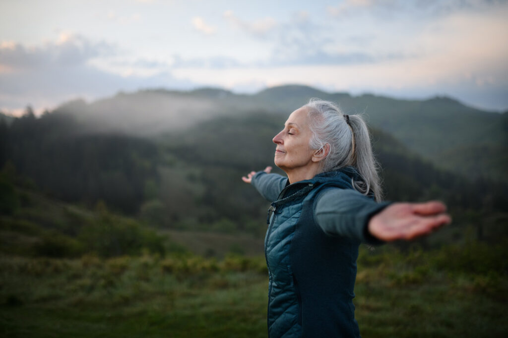 Senior woman expressing her gratitude outside in nature on a hike after reading inspiring gratitude quotes