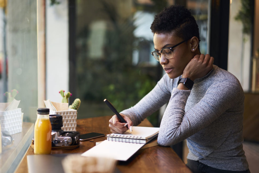 woman writing goals in journal at a cafe