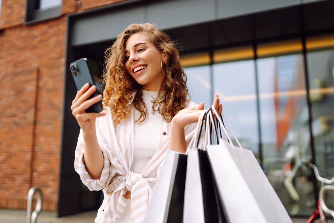 A woman with shopping bags looking at her phone.