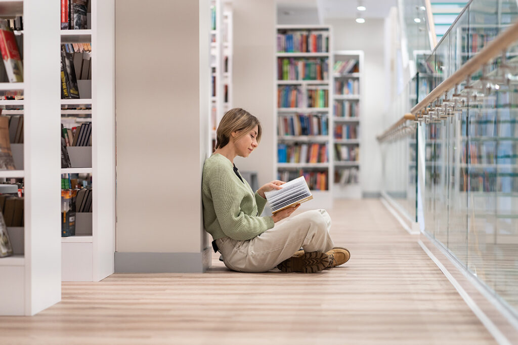 Woman sits on floor of library reading books on resilience
