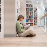 Woman sits on floor of library reading books on resilience