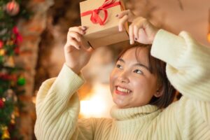 Asian woman in a white turtleneck smiling because she's holding gifts for people who work from home above her head