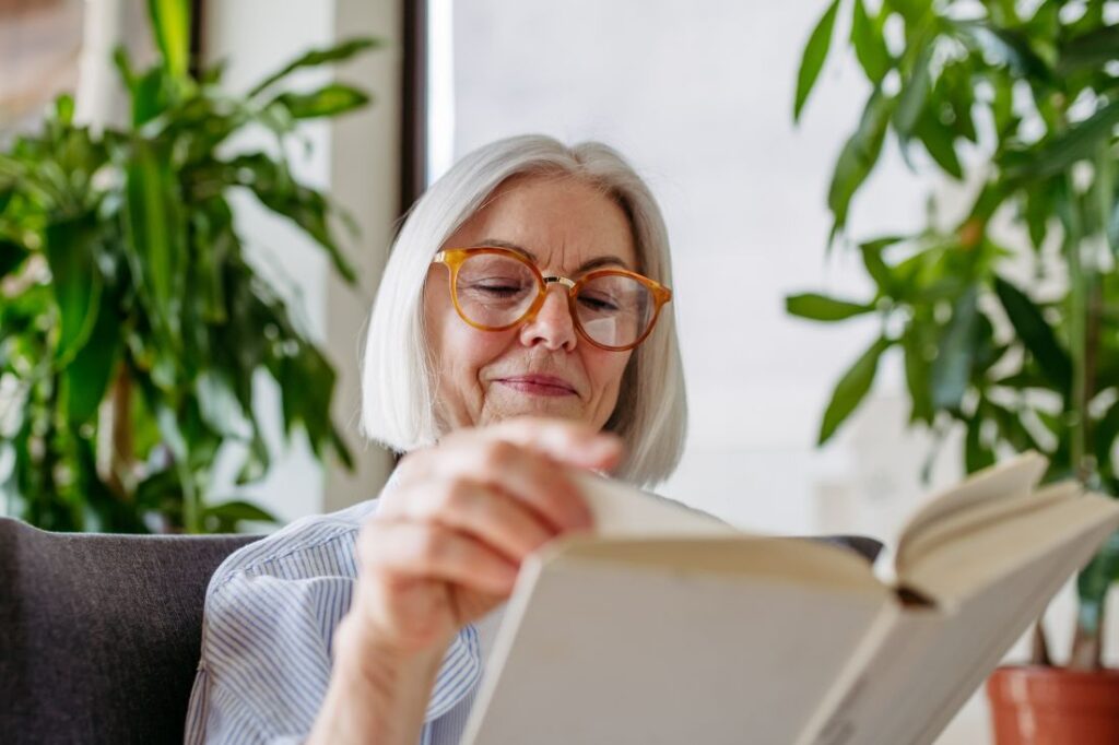 older woman with glasses sitting on a couch and flipping through a book