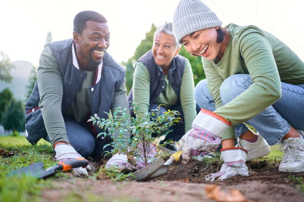 Three people smiling while gardening showing the benefits of volunteering