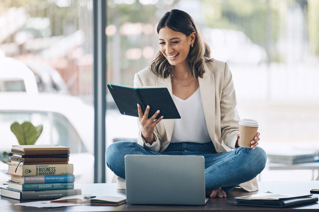 Business woman reading books about setting goals, sitting on her desk drinking coffee